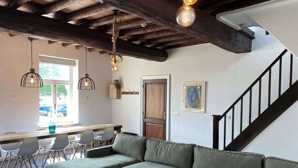 A cozy living area with a green sofa, wooden coffee table, and a dining table with chairs. A staircase with a black railing is visible. - Authentic house (6p) in prime location near Maastricht (Eijsden)
