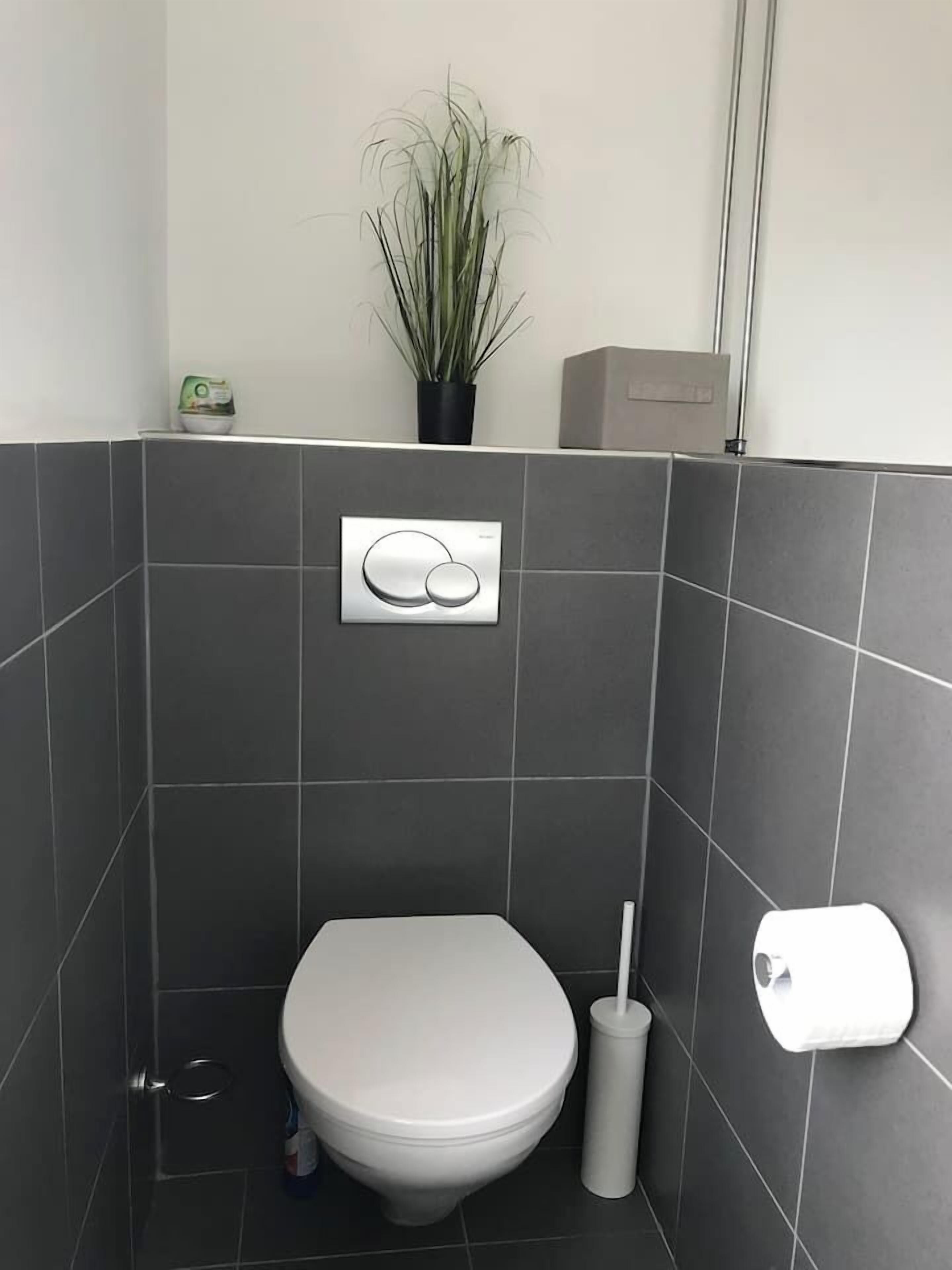 Une salle de bain moderne équipée de toilettes, d’un bidet et d’un système de chasse d’eau mural.