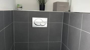 Une salle de bain moderne équipée de toilettes, d’un bidet et d’un système de chasse d’eau mural.