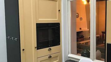 Eine Küchenzeile mit Mikrowelle, einem Schrank mit Schubladen, einem weißen Stuhl und einem Fenster mit Blick ins Innere.