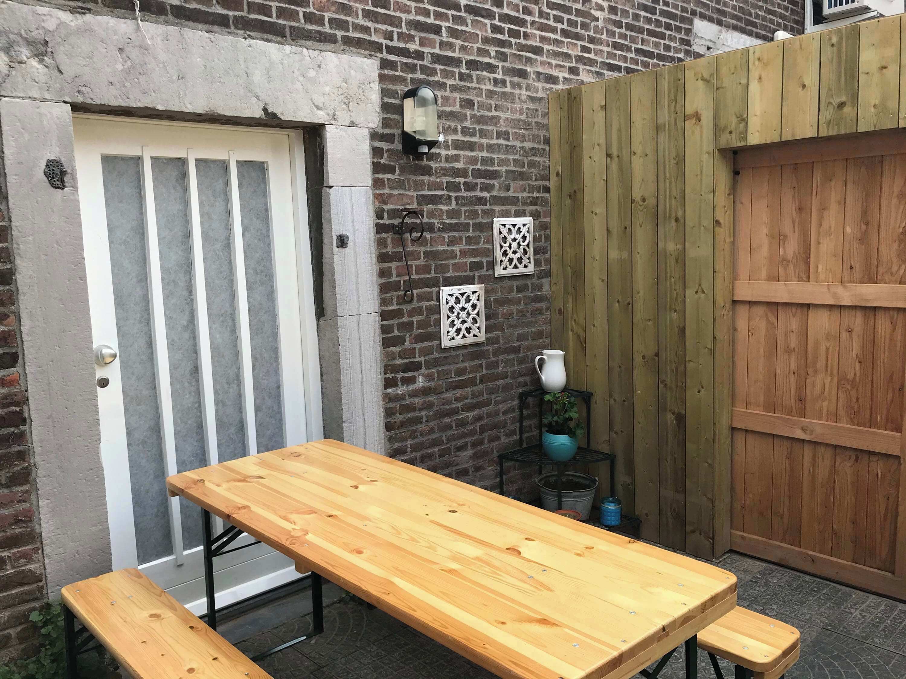 A wooden table with benches, a brick wall, a wooden gate, and a door with a window.