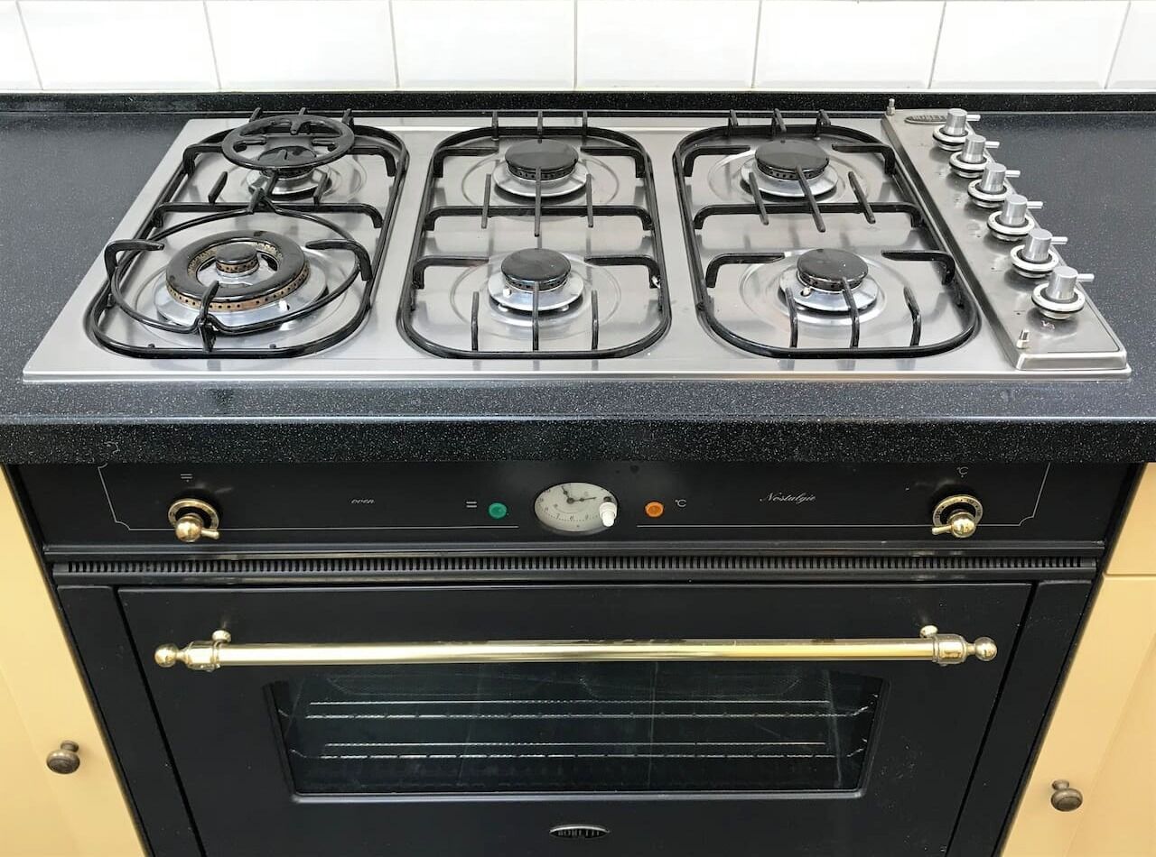 Een keuken met een gasfornuis, oven, en een bedieningspaneel met knoppen en een draaiknop.