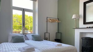 Una cama bien hecha con almohadas, una lámpara de noche y vistas al exterior.