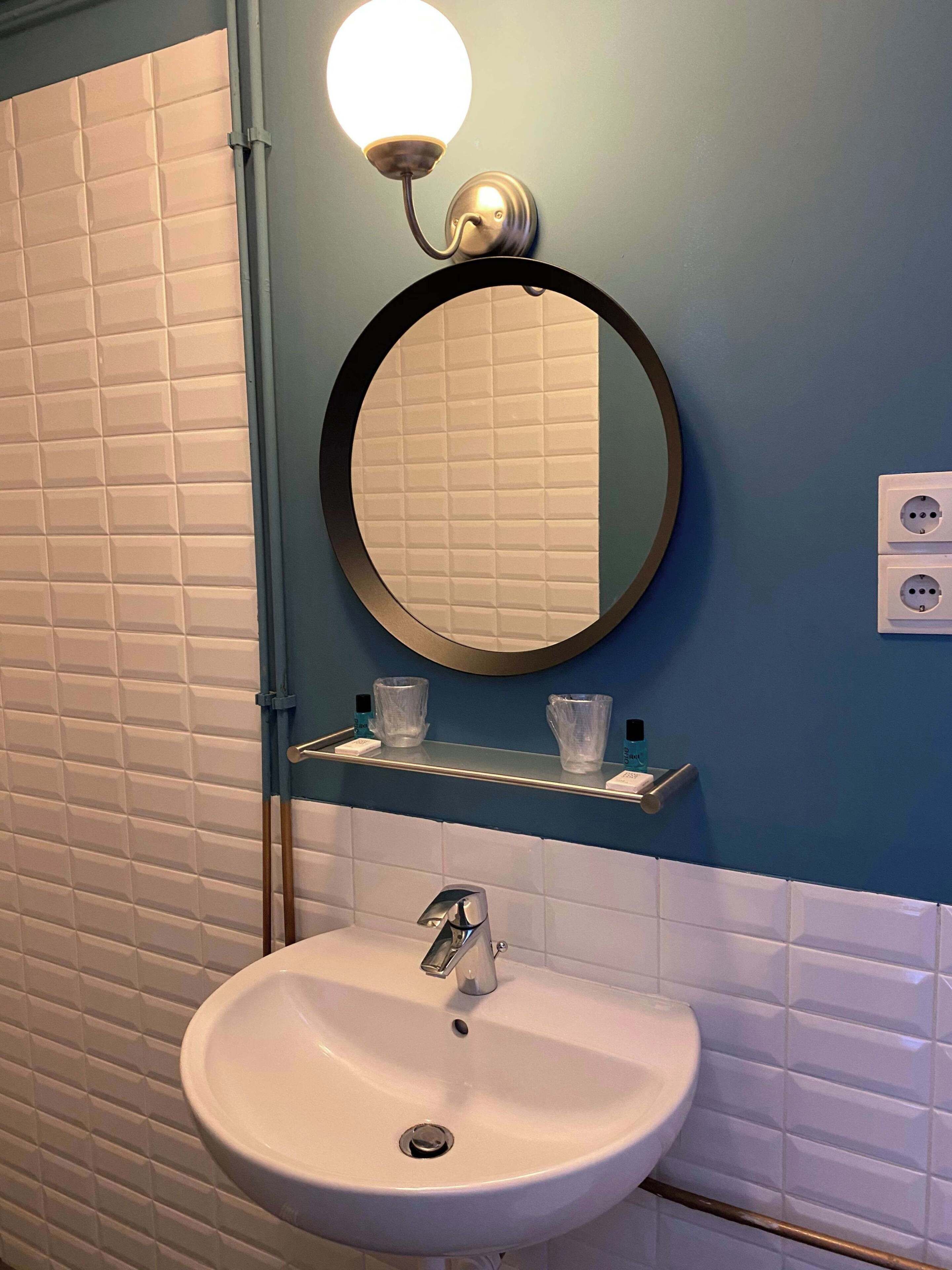 Une salle de bain avec un lavabo blanc, un miroir rond et un luminaire fixé au mur.