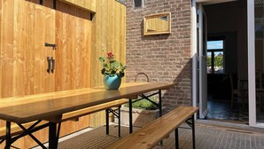 Una mesa de madera al aire libre con bancos, una planta en maceta y una pared de ladrillo.