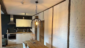 Une cuisine moderne avec des meubles blancs, une table à manger en bois et un luminaire suspendu.
