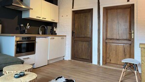 Une cuisine moderne avec des meubles blancs, un four encastré et une machine à café. On y trouve deux portes en bois et un petit tabouret.