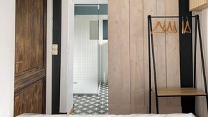Une pièce avec une porte en bois, une porte coulissante de style grange, un portant en métal avec des cintres en bois et un sol carrelé.