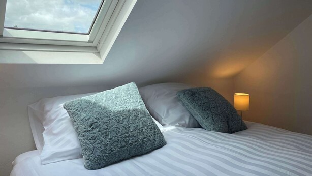 A bedroom with a skylight, a bed with white bedding, two pillows, and a bedside lamp. - Cozy apartment (4p) prime location near Maastricht (Eijsden)