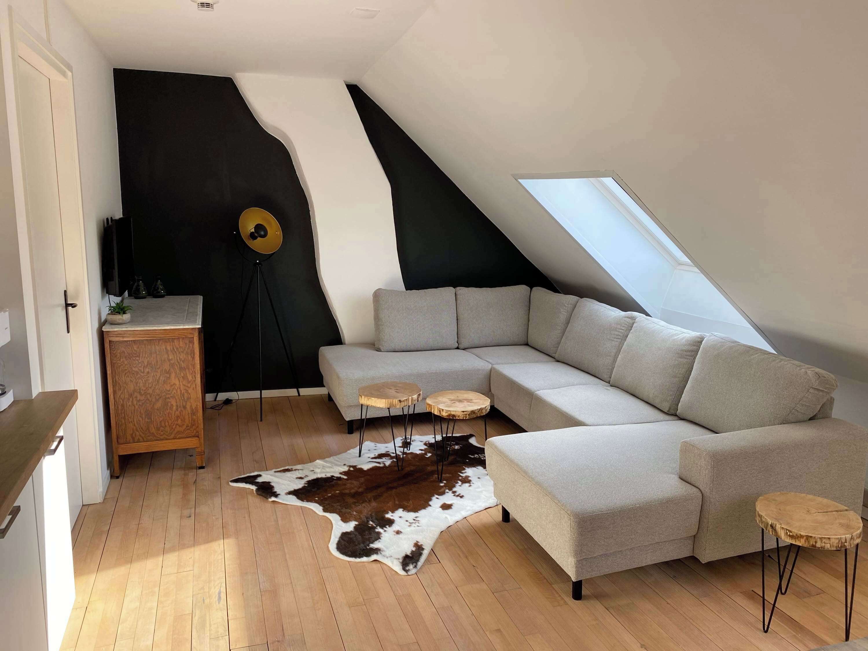 Een moderne loft met een schuine plafond, een hoekbank, een koehuiden vloerkleed en een vloerlamp.
