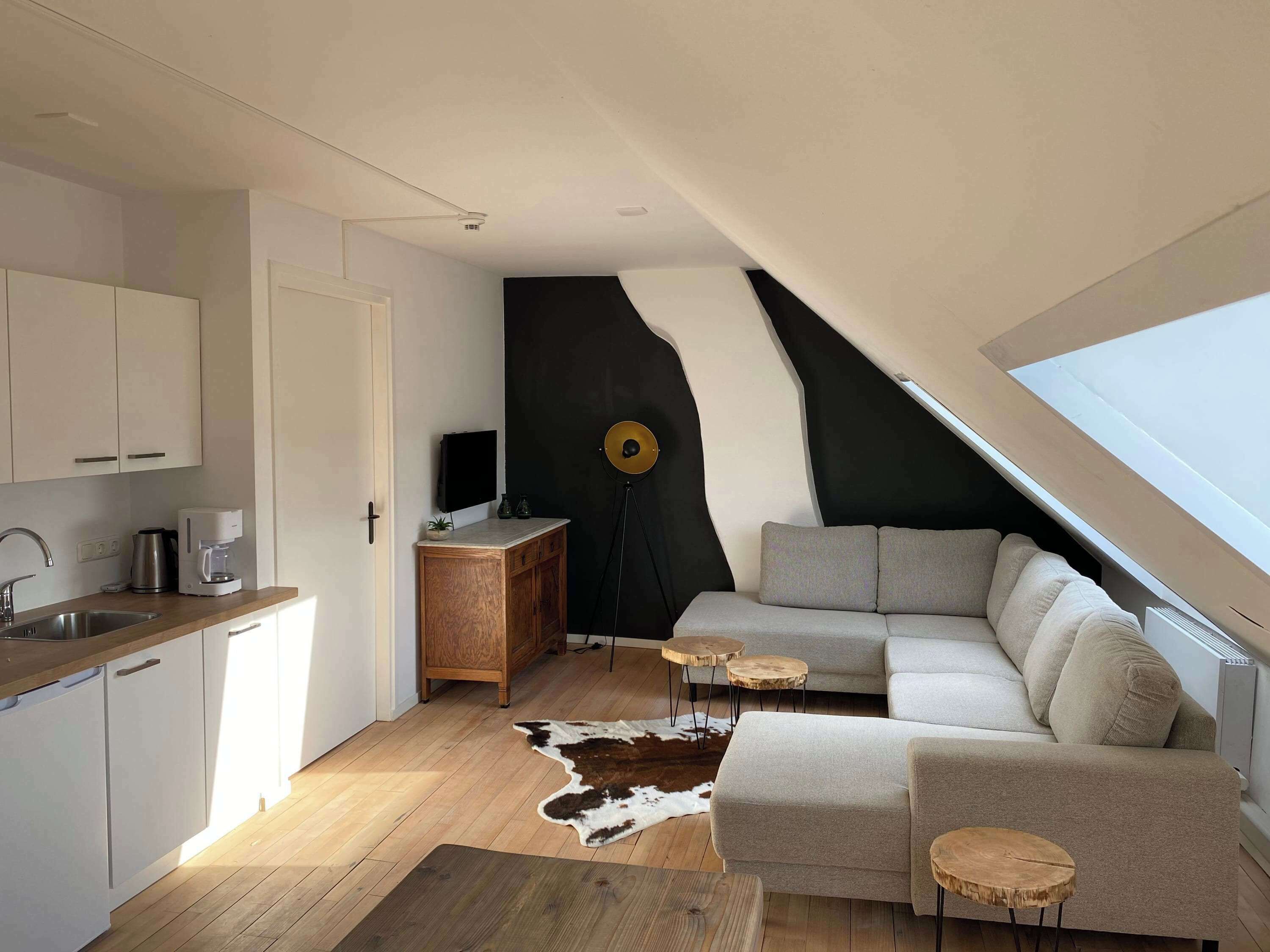 A modern loft with a kitchen, a living area with a sofa and coffee table, a black accent wall, and a skylight.