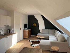 A modern loft with a kitchen, a living area with a sofa and coffee table, a black accent wall, and a skylight.