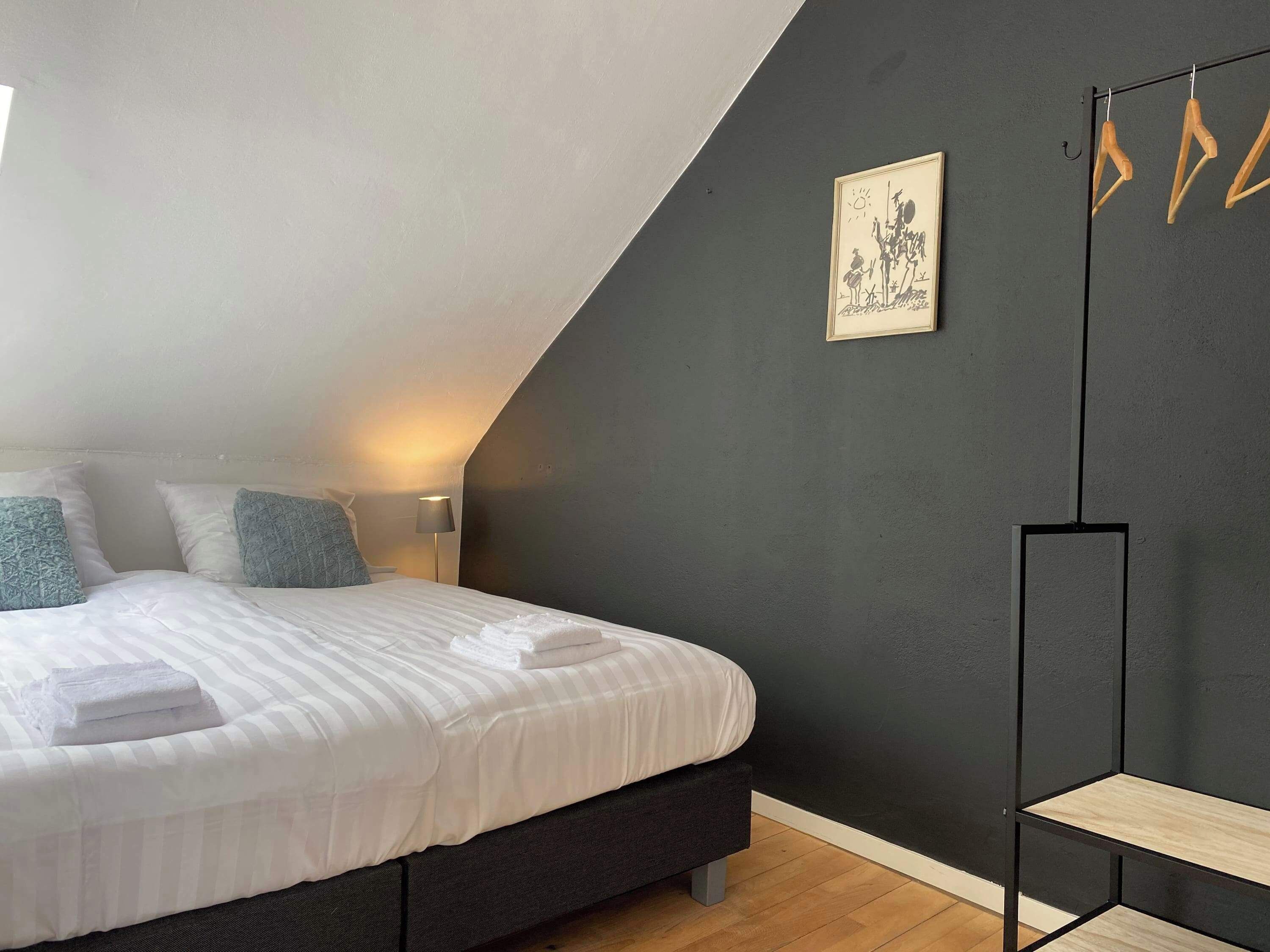 Une chambre à coucher avec un lit, des oreillers, une lampe de chevet, un mur de couleur sombre et un tableau encadré.