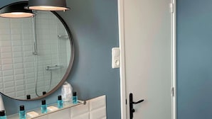 A bathroom with a white sink, a round mirror, a shower, and a door with a black handle. - Atmospheric apartment (5p) in toplocation near Maastricht (Eijsden)