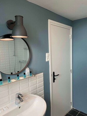Un baño con lavamanos blanco, un espejo redondo, ducha y una puerta con pomo negro.
