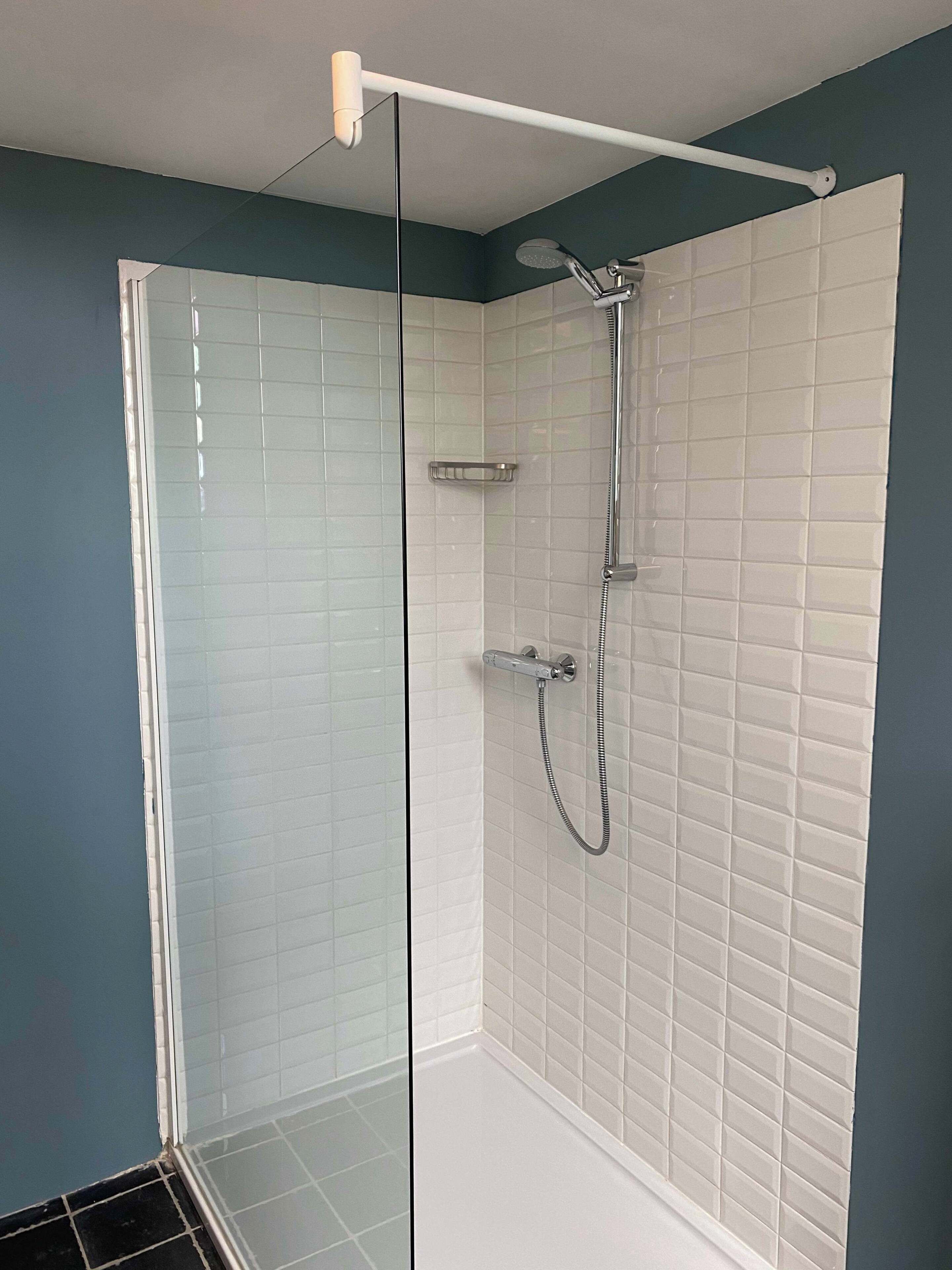 Une douche fermée par des parois de verre, avec des murs recouverts de carreaux blancs, une douchette à main et un robinet fixé au mur.