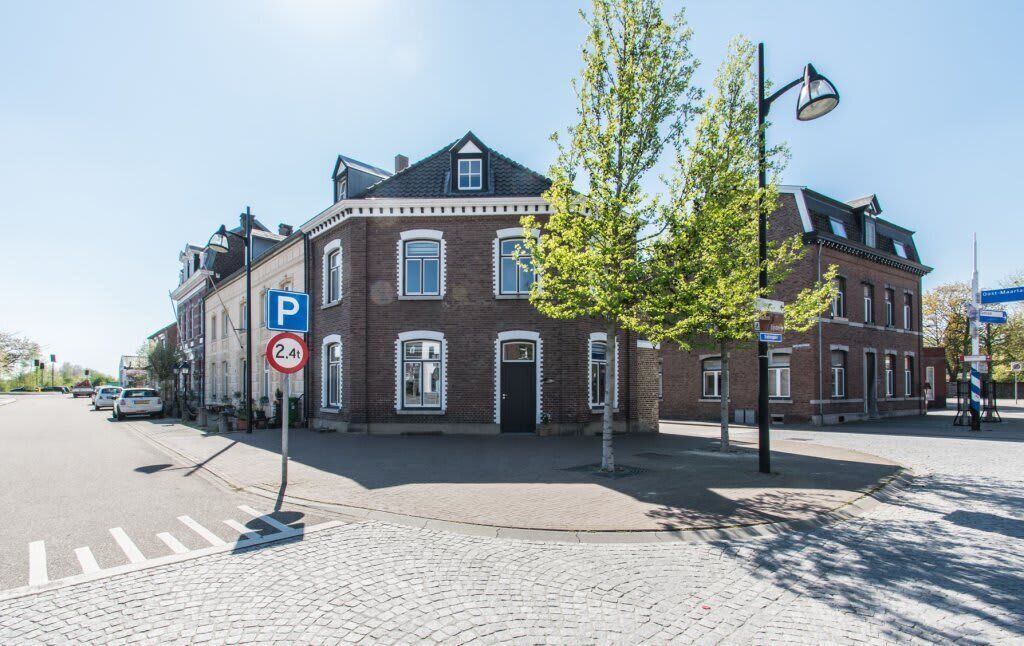 A historic building with a brick facade, a parking sign, and a tree in front.