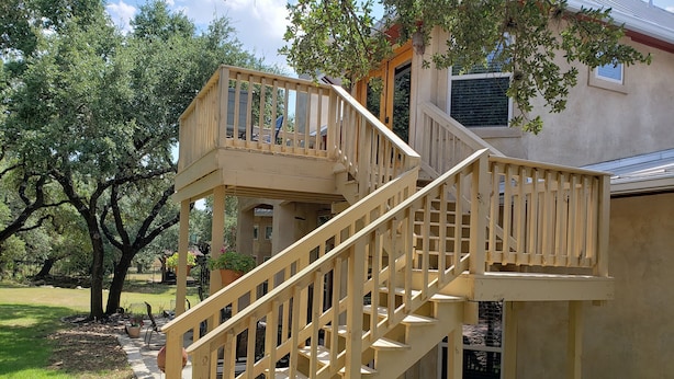 Una escalera de madera que conduce a un balcón con vistas a una casa y árboles circundantes.