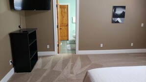 Un dormitorio con cama, televisor, puerta de madera y un cuadro en la pared.