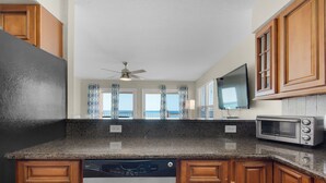 A kitchen with granite countertops, wooden cabinets, a dishwasher, a microwave, and a ceiling fan. - Gulf Front Condo, Modern Coastal Vibe, Sleeps 6 + Free Attraction Tickets! (Santa Rosa Beach)