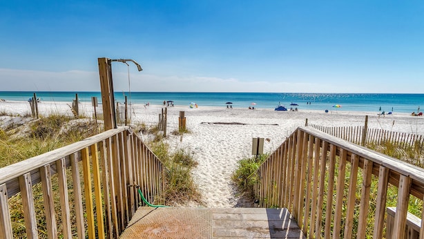 A wooden boardwalk leading to a sandy beach with umbrellas and people in the distance. - Gulf Front Condo, Modern Coastal Vibe, Sleeps 6 + Free Attraction Tickets! (Santa Rosa Beach)