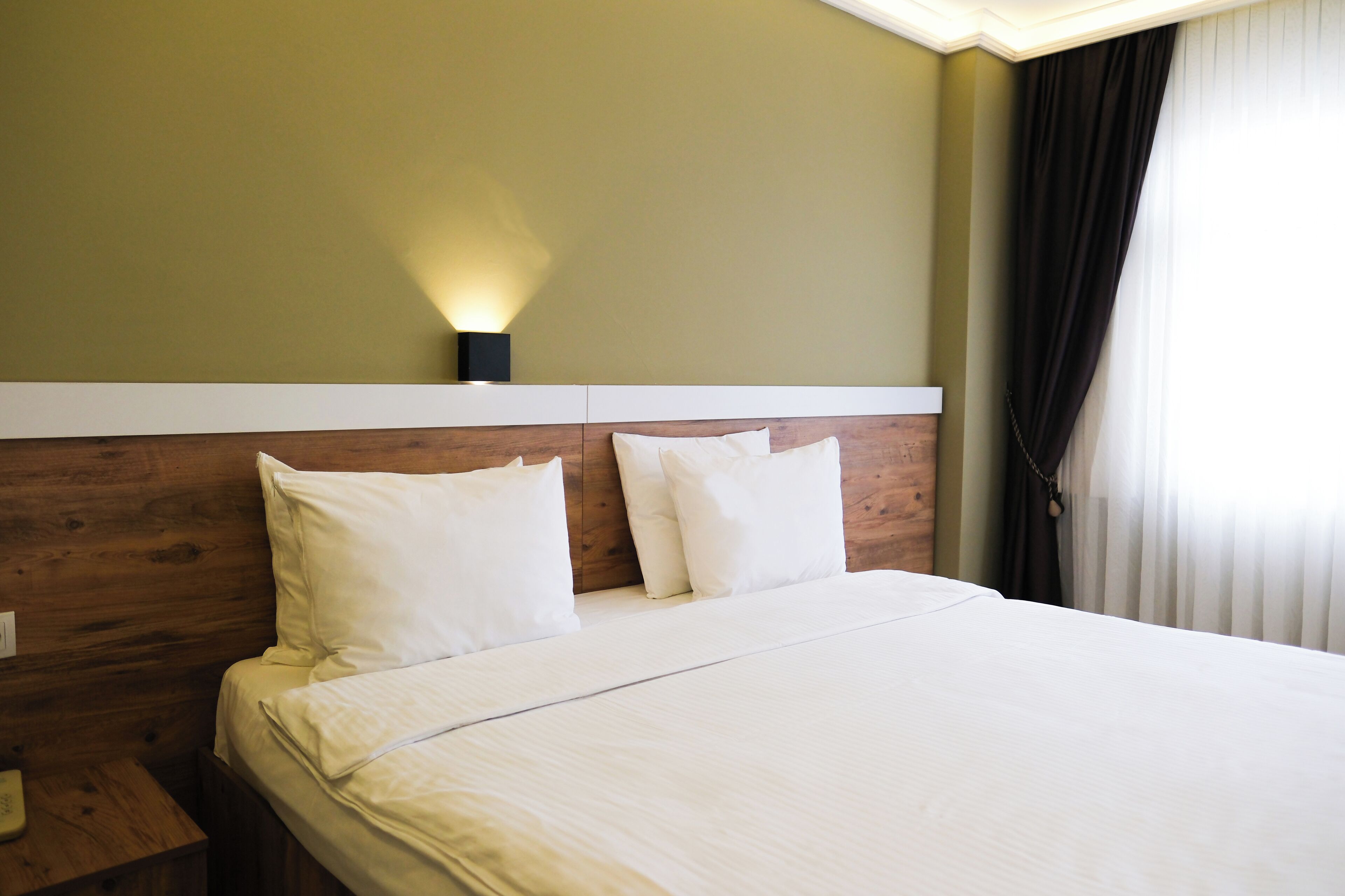 A hotel room with a wooden headboard, a bed with white linens, and a nightstand with a lamp.