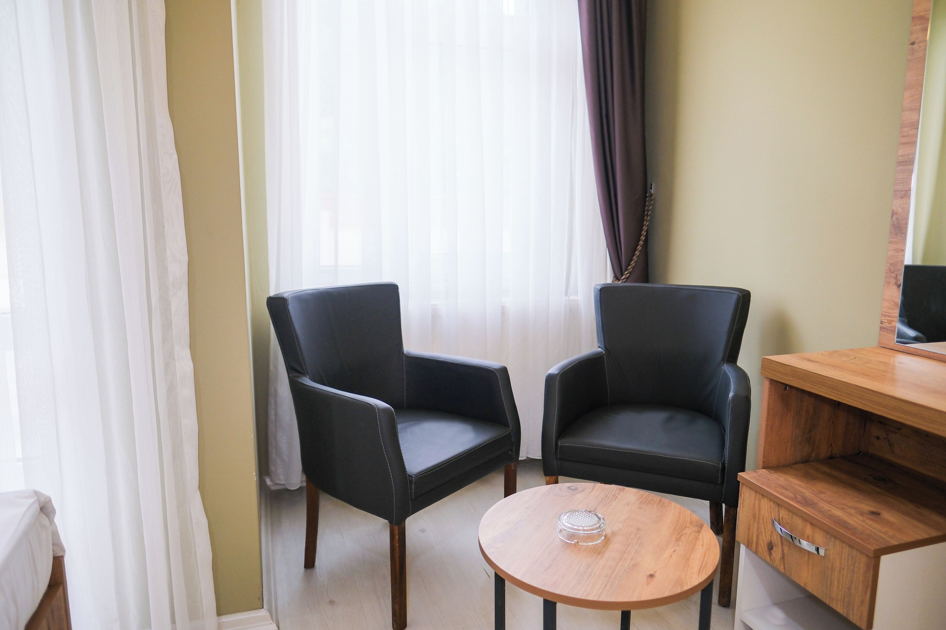 Una habitación con dos sillones de cuero negro, una mesa de madera con un objeto de vidrio, un escritorio de madera y una cama con cubrecama blanco.