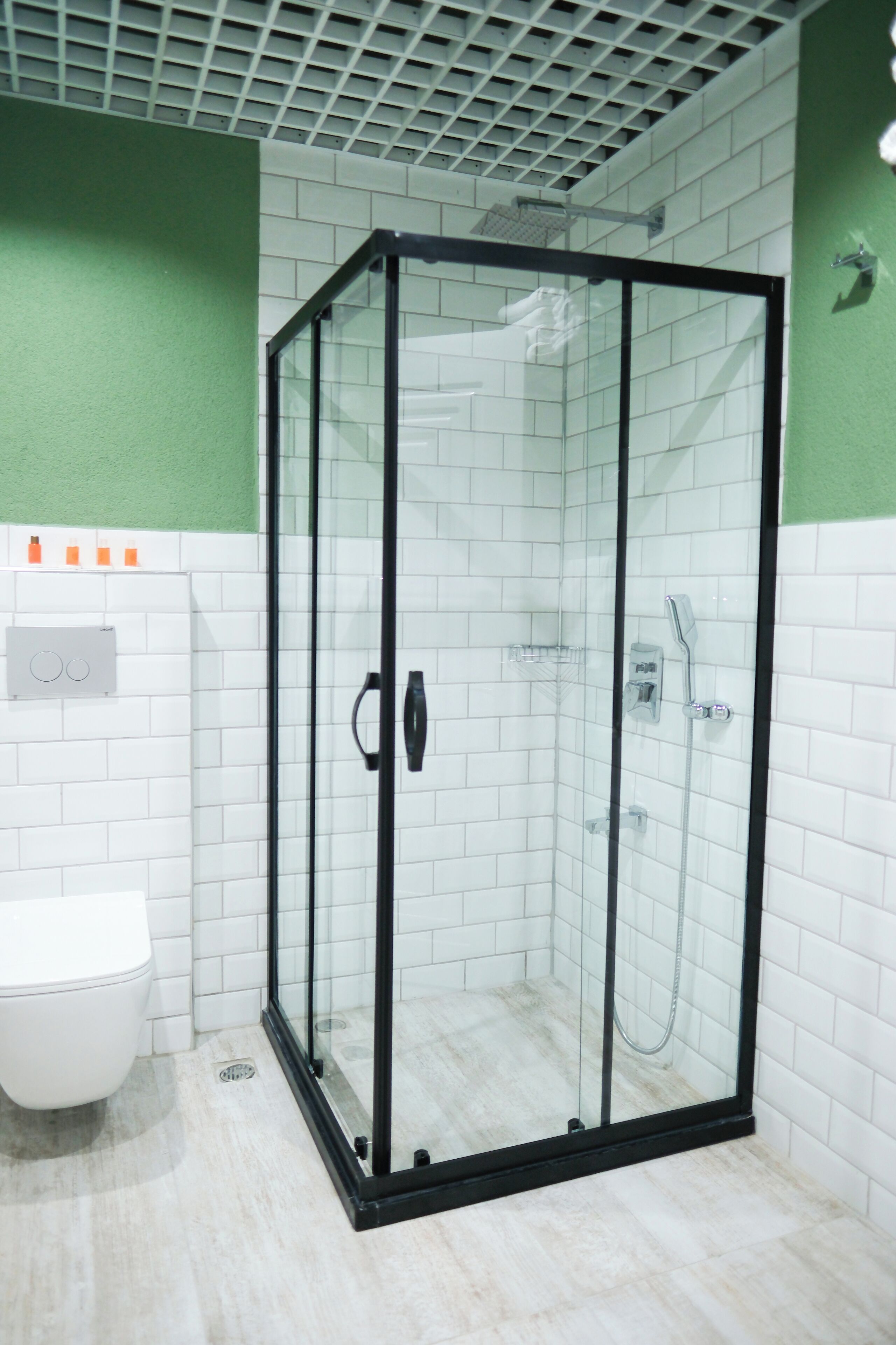 Ducha con cerramiento de vidrio, marco negro, paredes de azulejos blancos y una pared de acento verde.