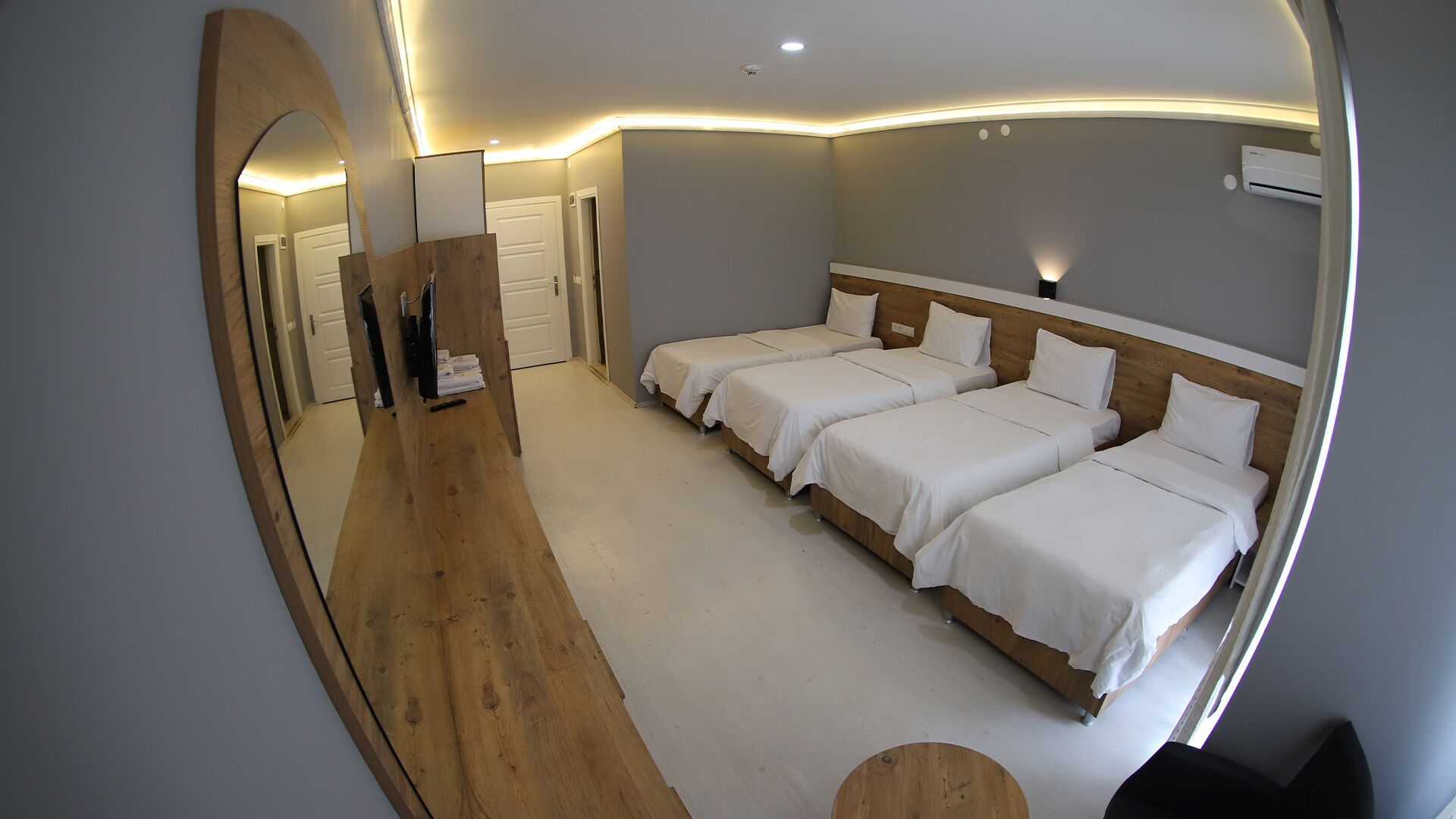 A modern hotel room with a large mirror, two single beds, a wooden floor, and a small round table.