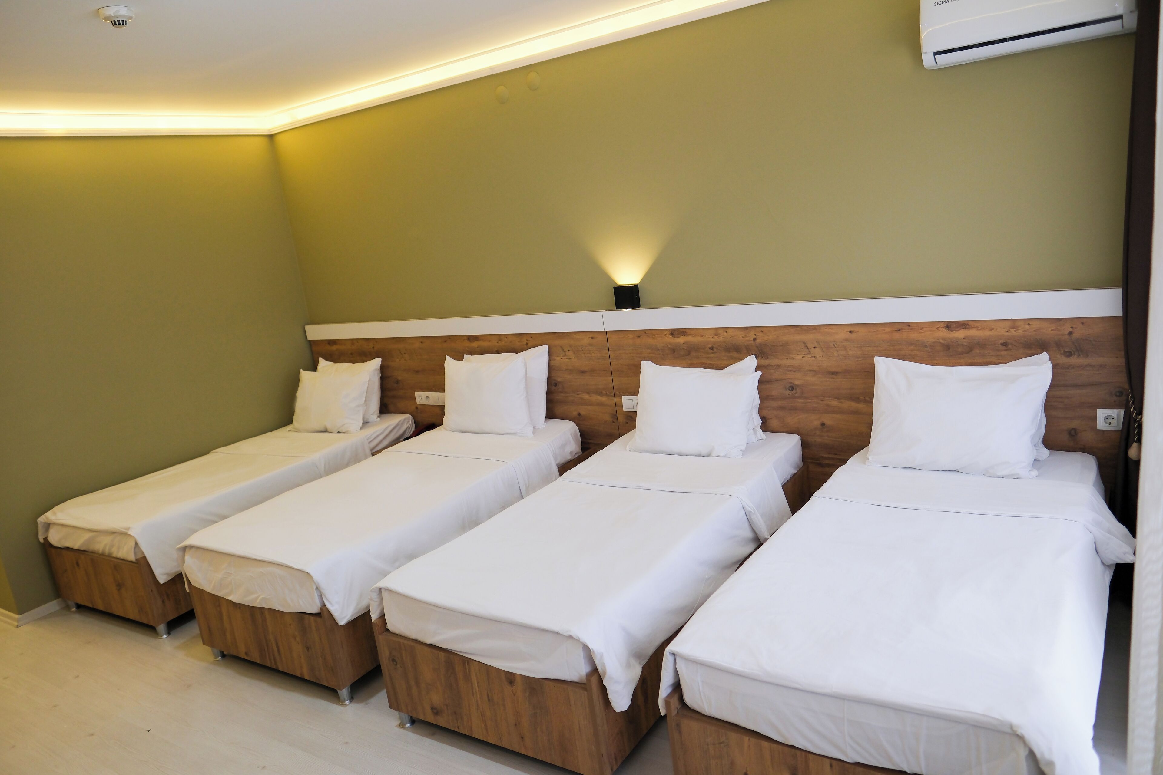 Een hotelkamer met vier enkele bedden, houten hoofdborden en een wandairconditioner.