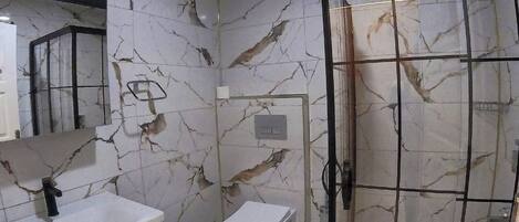 A bathroom with a marble floor, a glass shower enclosure, a toilet, and a sink with a mirror.