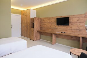 Una habitación de hotel con un armario de madera, un televisor de pantalla plana en una pared de madera, una mesita redonda y dos camas.