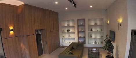Un vaste espace de vie agrémenté d’un canapé moderne, d’une table basse et d’étagères intégrées. Un escalier avec une rampe est visible au premier plan.