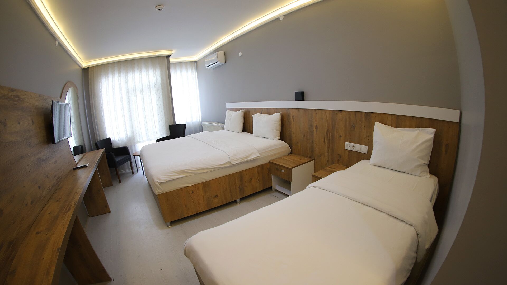 A hotel room with two beds, a wooden desk, a chair, a television, and a window with curtains.
