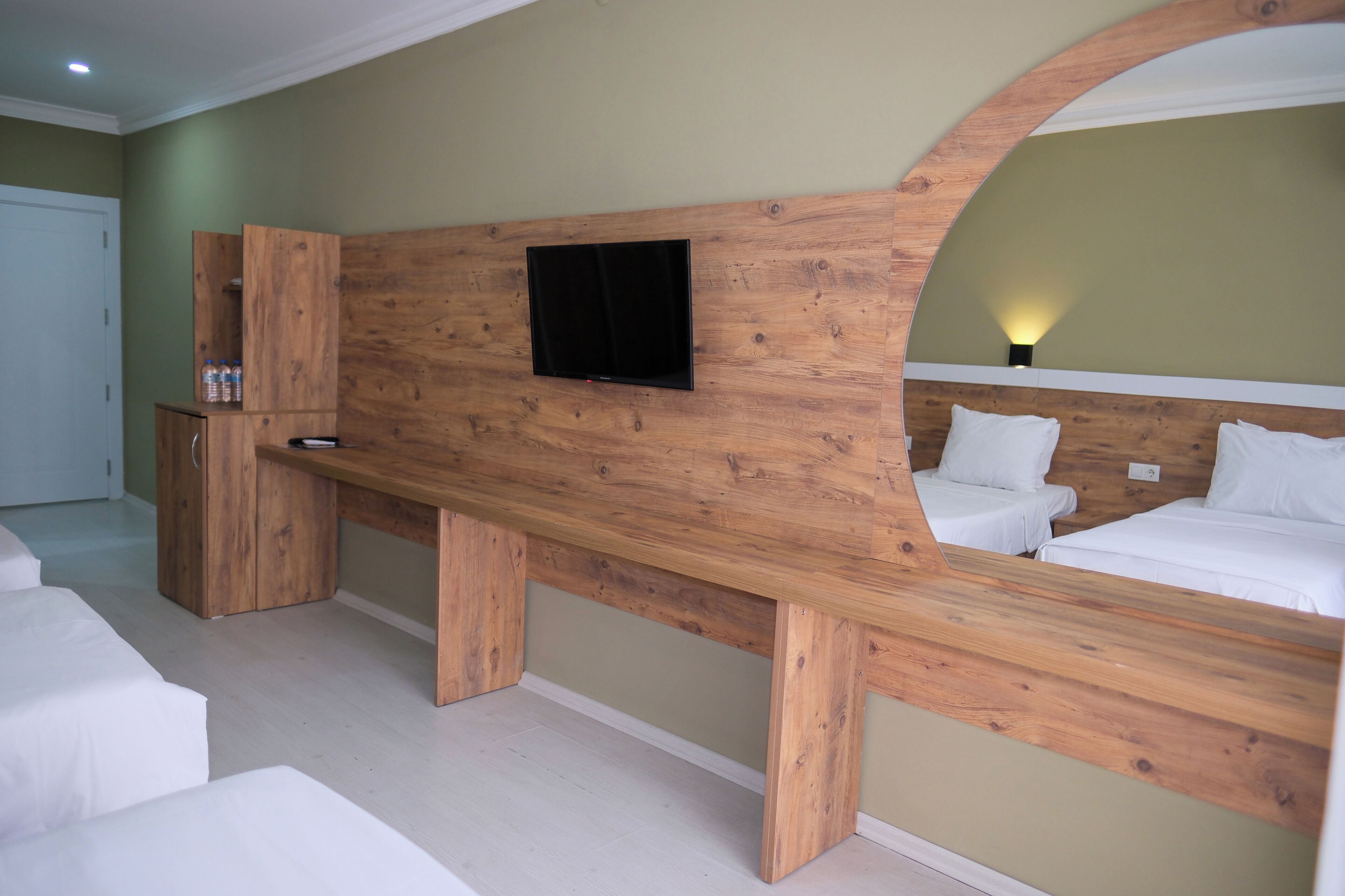 A bedroom with a wooden headboard, a flat-screen TV mounted above a bed, and a wooden bench with a mirror.