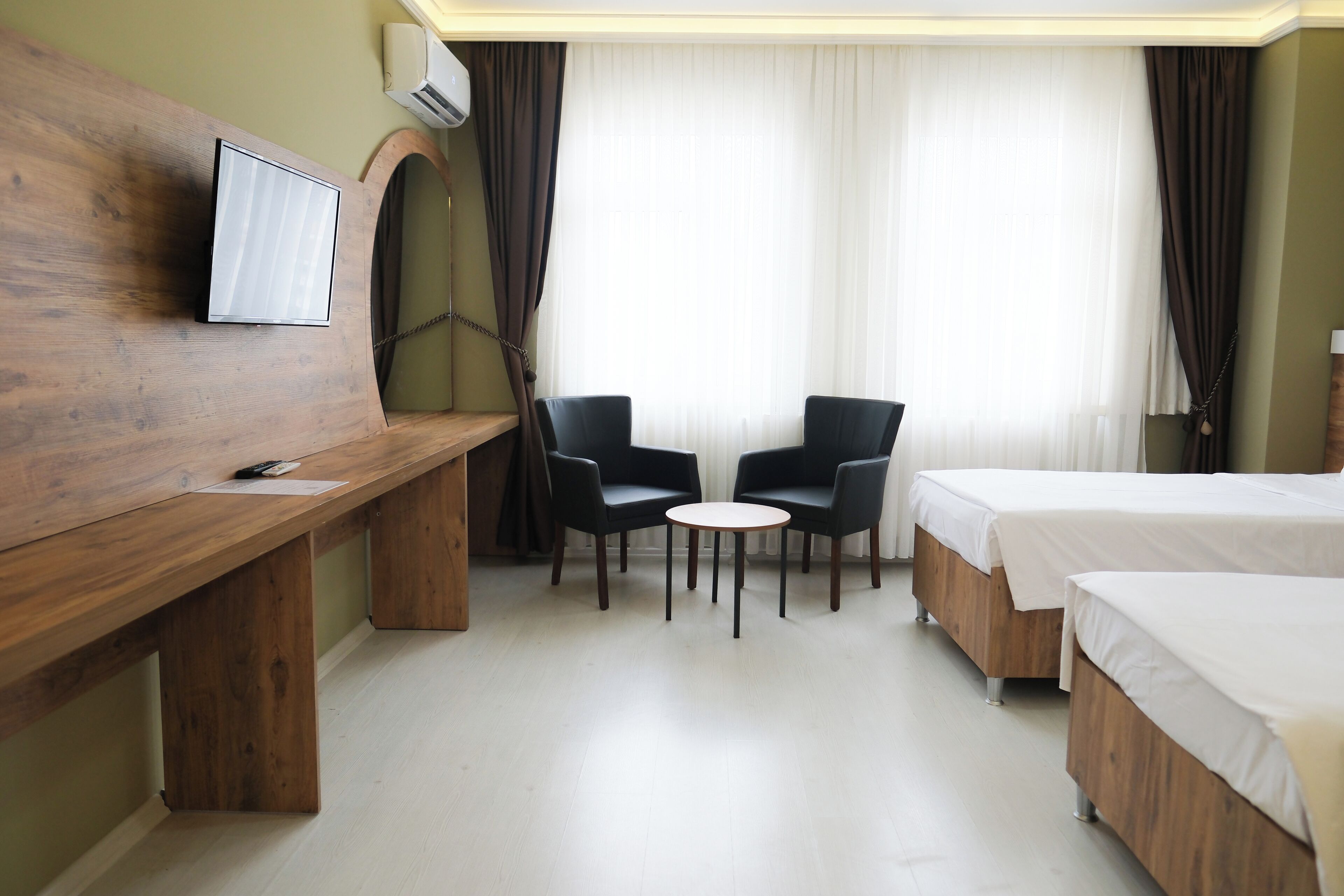 A hotel room with a wooden desk, two black chairs, a small round table, and two beds.