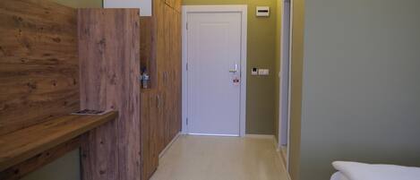 A narrow hallway with wooden cabinets, a white door, and a bed with a white cover.