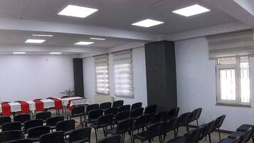 A conference room with rows of black chairs, white tables with red tablecloths, and large windows with blinds.