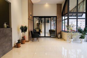 A modern hotel lobby with a glass door leading to a staircase, potted plants, and a seating area. - Altayhan Hotel (Amasya)