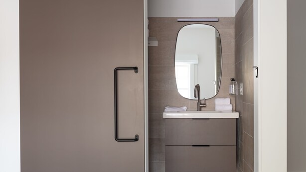 A bedroom with a bed, a sliding door leading to a bathroom with a sink and mirror.