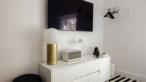 A modern, minimalist room with a white dresser, a flat-screen TV mounted above it, a round table lamp, and a black and white checkered rug.
