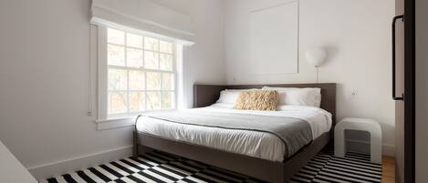 Un dormitorio con cama, ventana, mesita de noche y piso a cuadros blanco y negro.