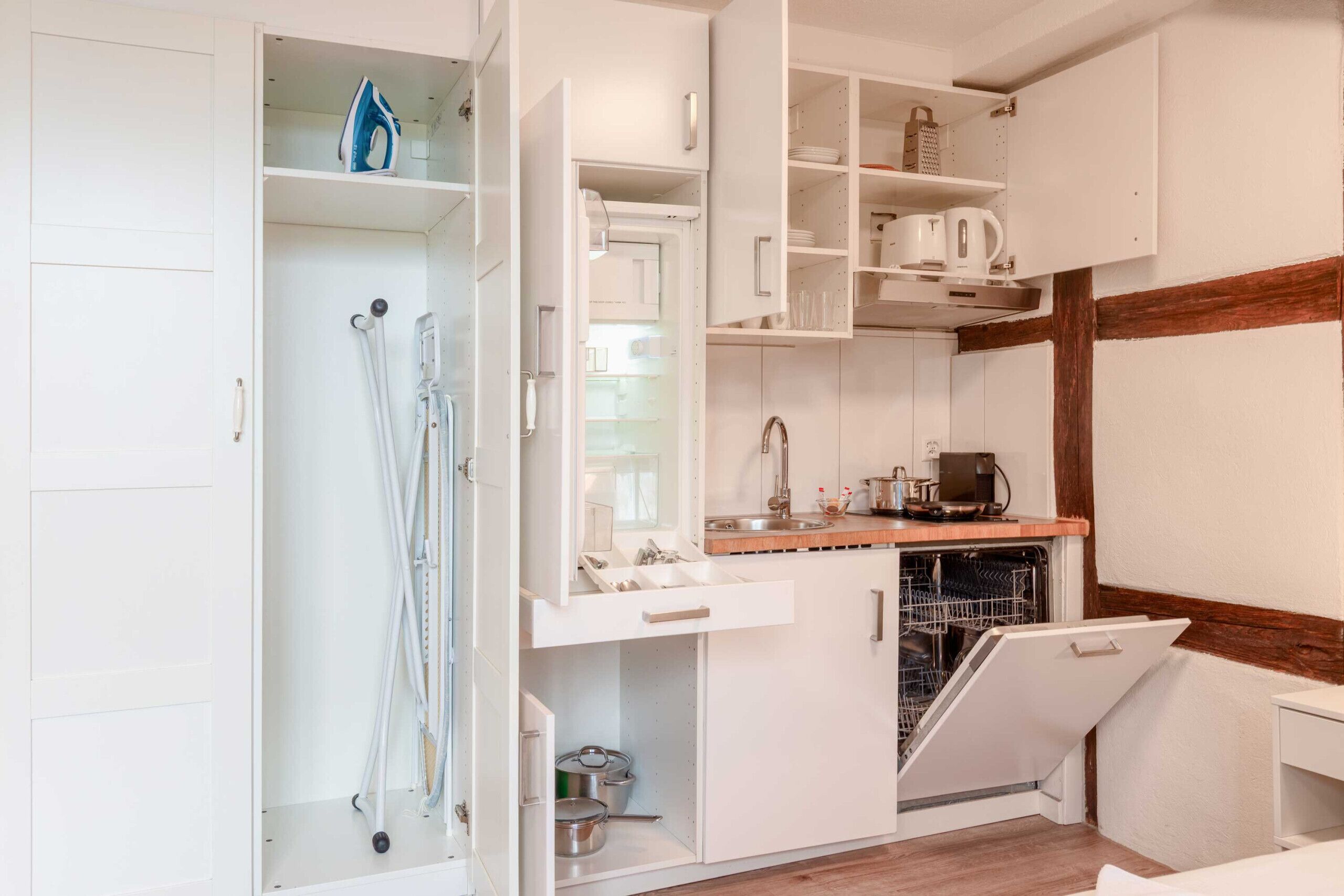 A compact kitchen with white cabinetry, a built-in dishwasher, and a wooden countertop.