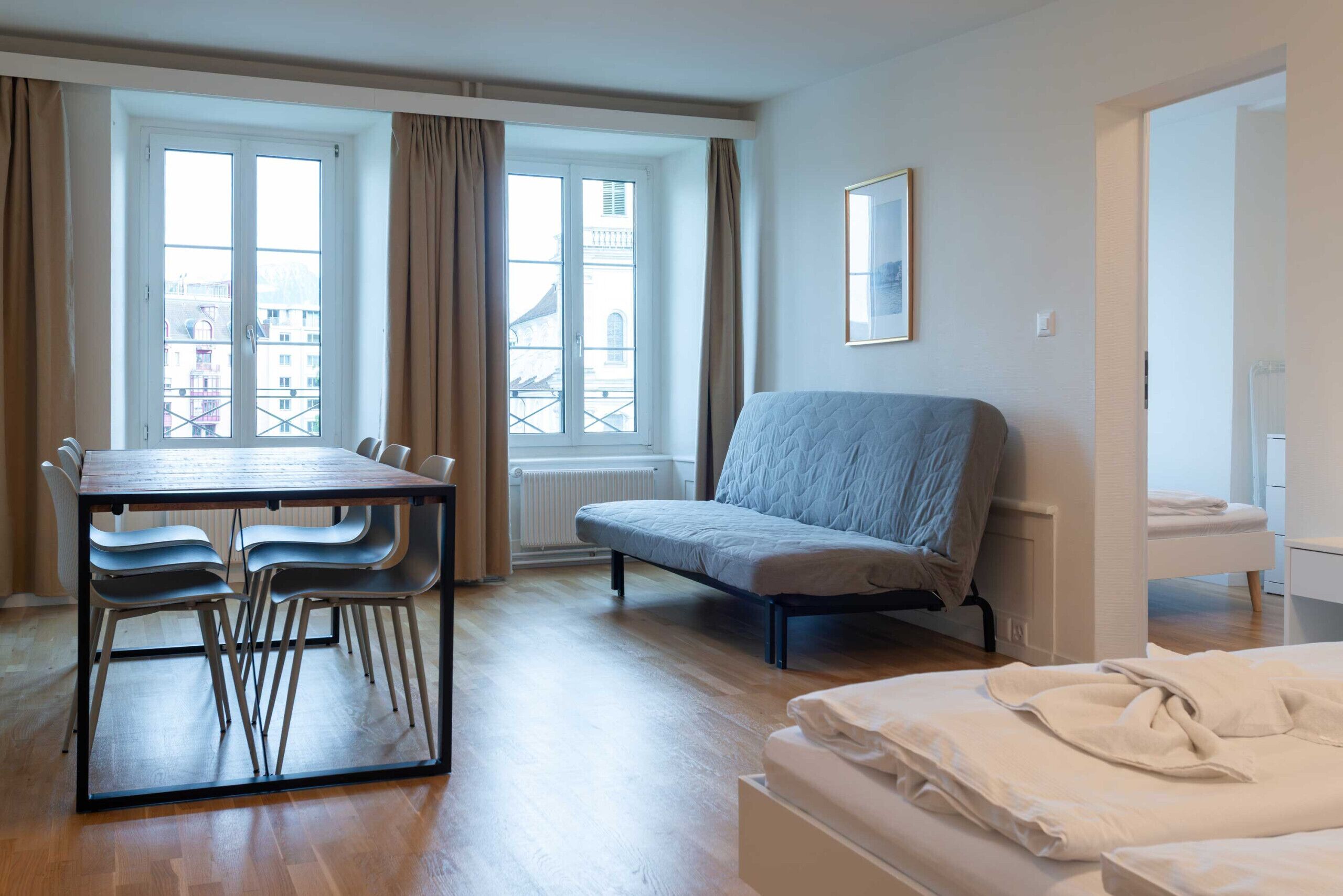 Una habitación con cama, una mesa con sillas, una ventana con cortinas y un radiador.