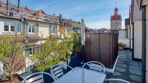 A courtyard with a table and chairs, a wooden shed, and a clock tower in the background. - Hitrental Chapel Bridge Apartments (Lucerne)