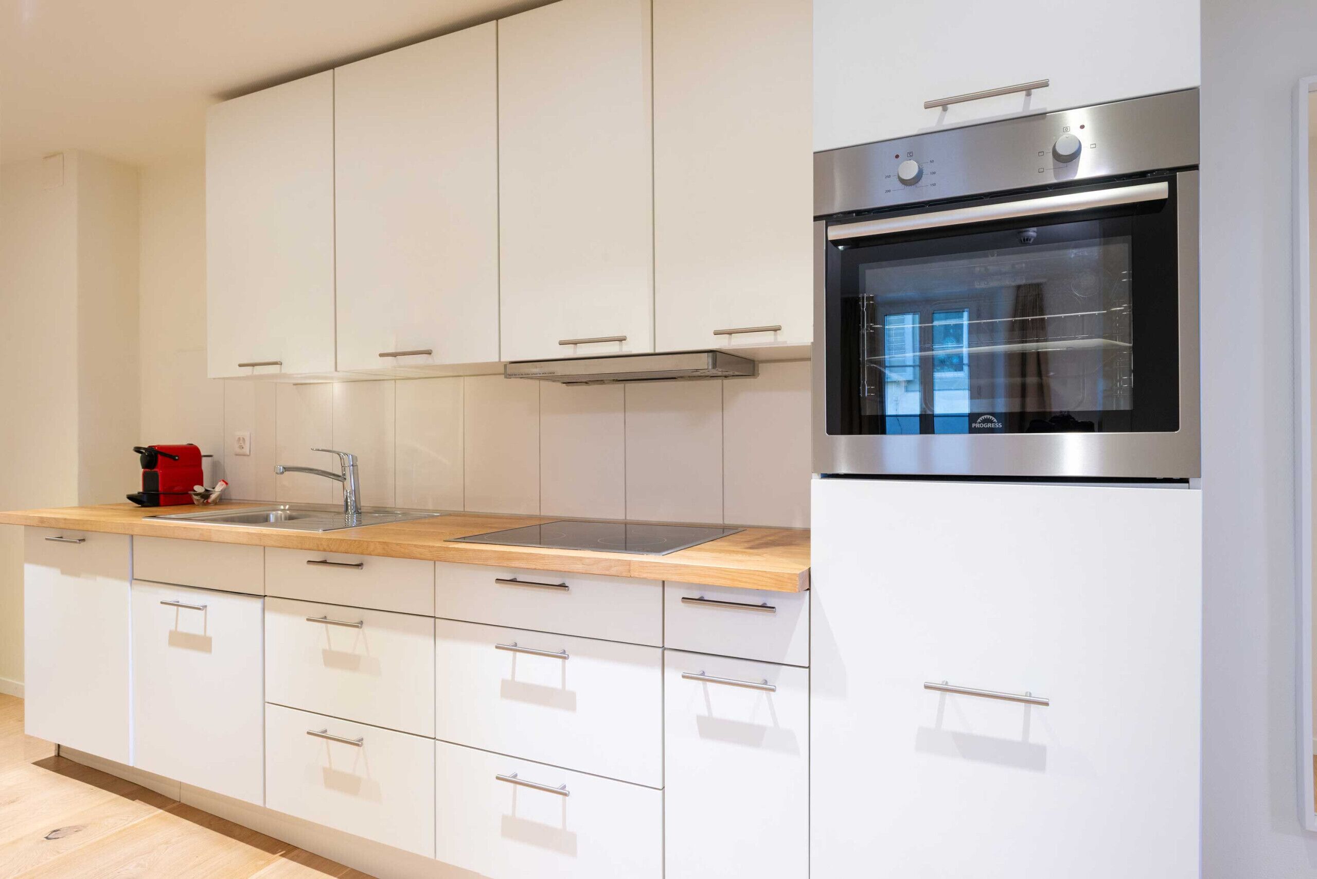 A modern kitchen with white cabinets, a stainless steel oven, and a wooden countertop.