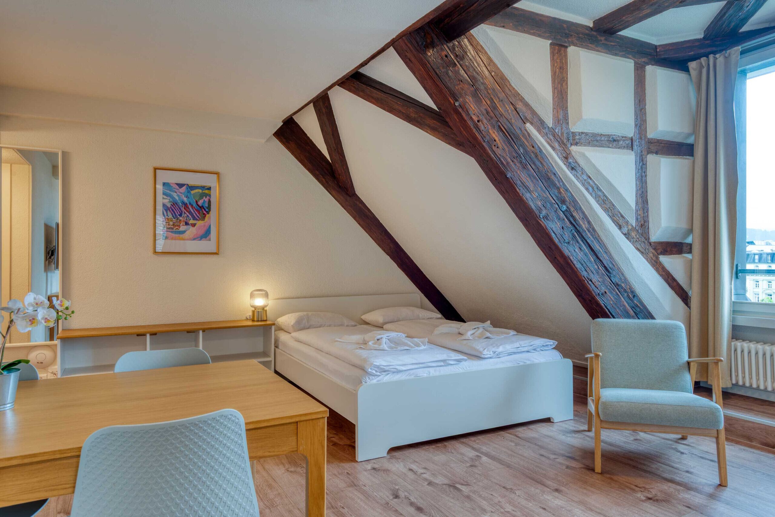 Una camera da letto con soffitto a falde, un letto, una sedia, un tavolo e una finestra.