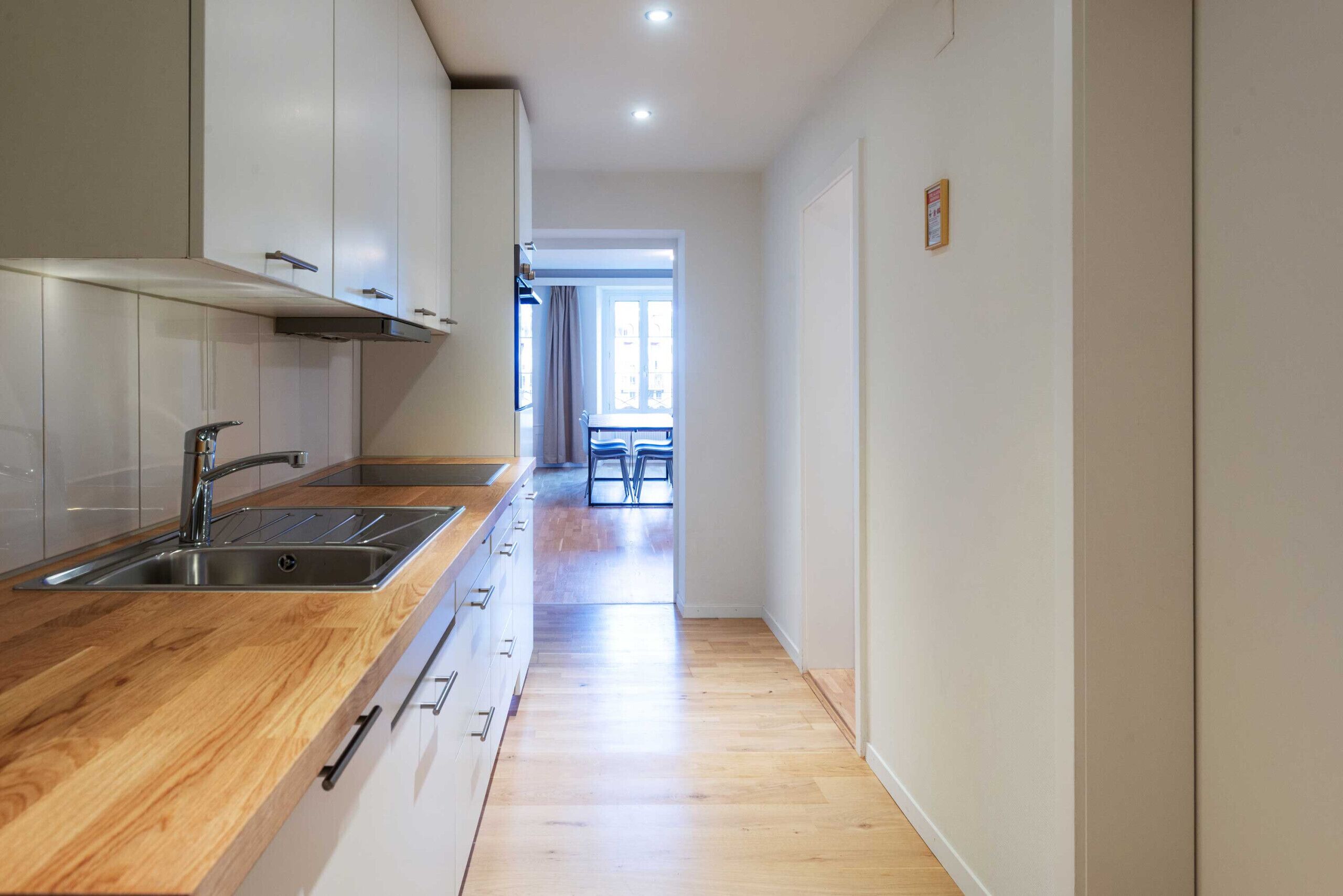 Una cocina moderna con encimera de madera, pileta de acero inoxidable y muebles blancos.