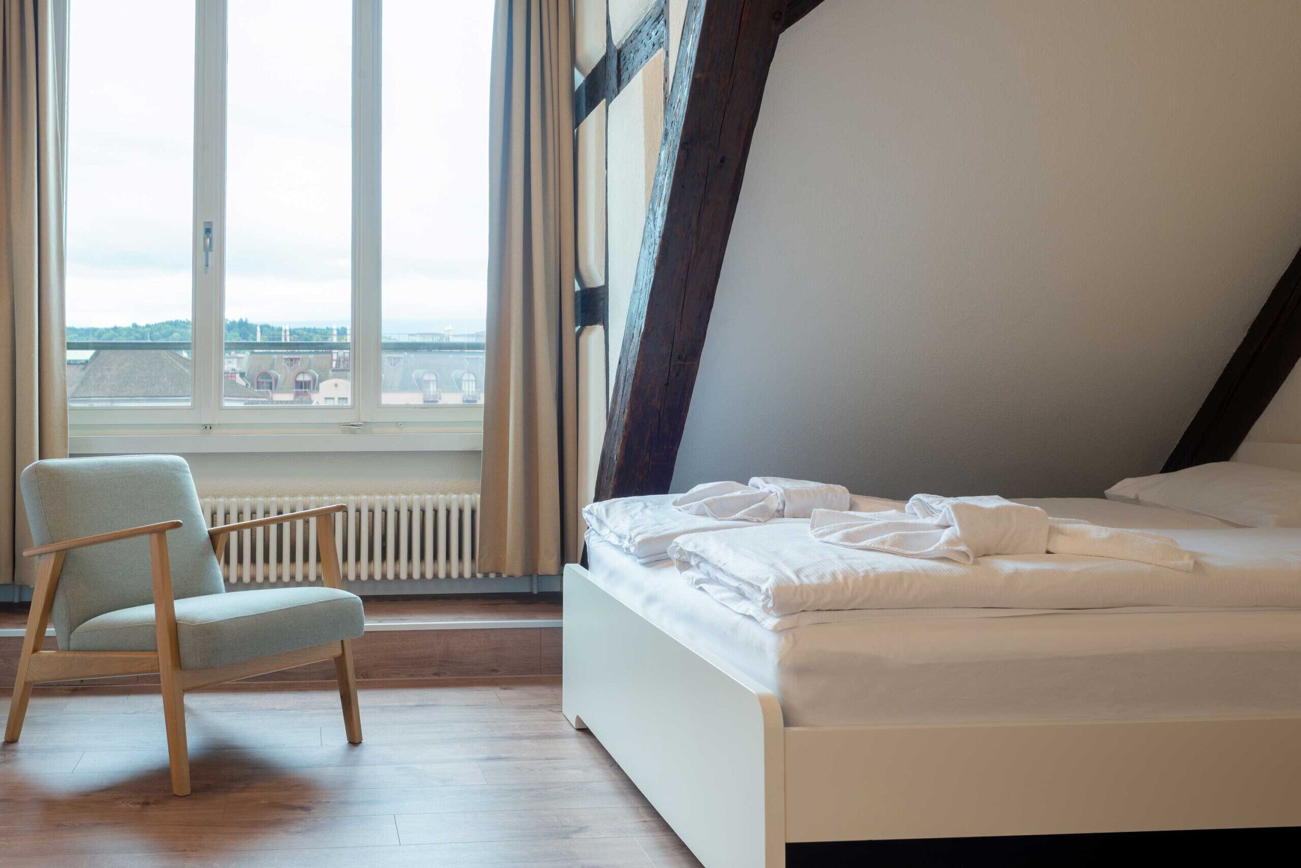 A bedroom with a bed, a chair, a window with a view, and a radiator.