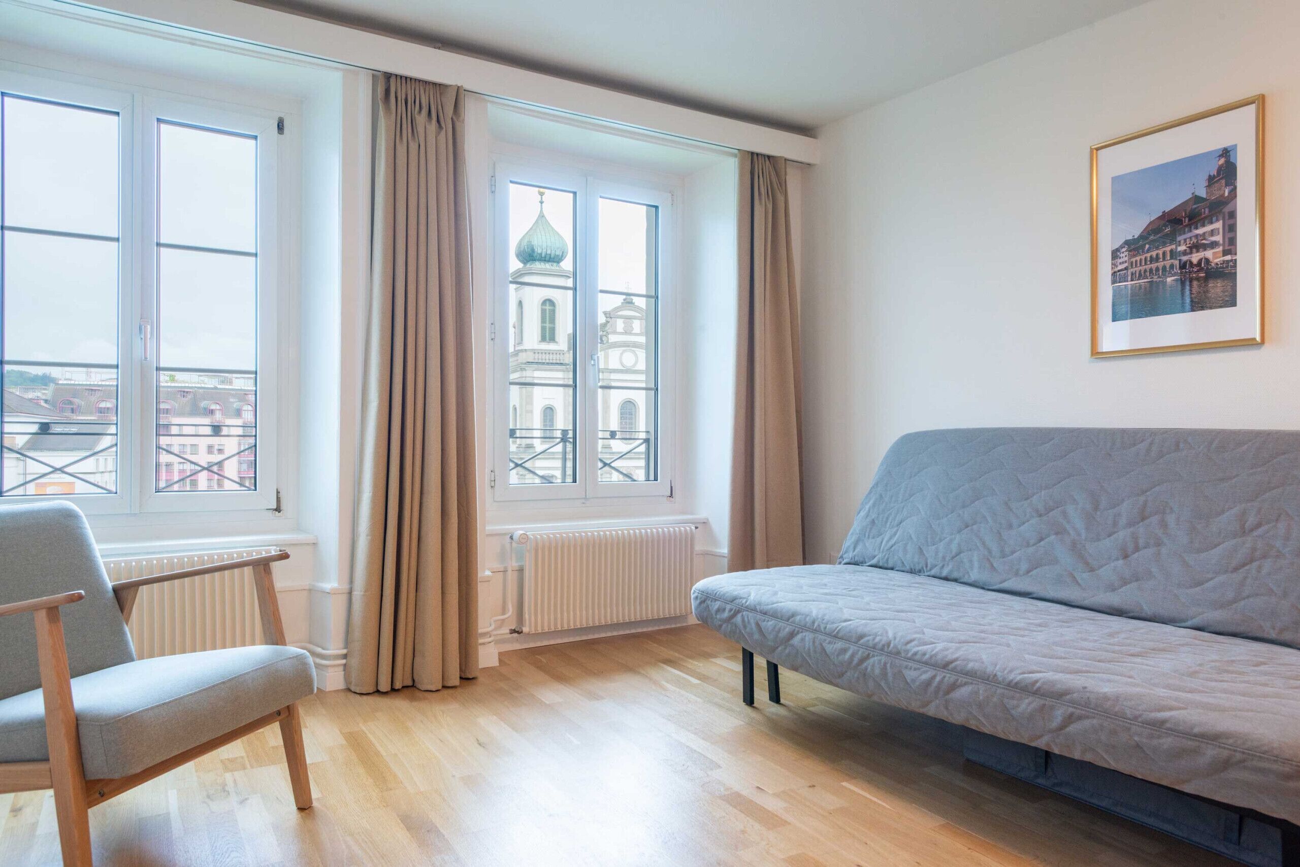 Una habitación con sofá, sillón, radiador y ventana con cortinas.